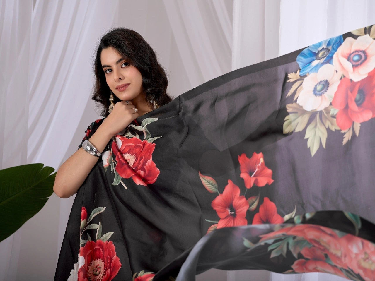 Woman holding a black saree with floral patterns against a white curtain background